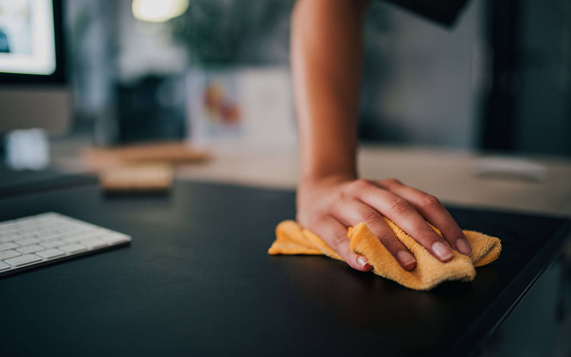 Close-up image of a female person cleaning black desk in modern office Close Up Image Of A Female Person Cleaning Black Desk In Modern Office